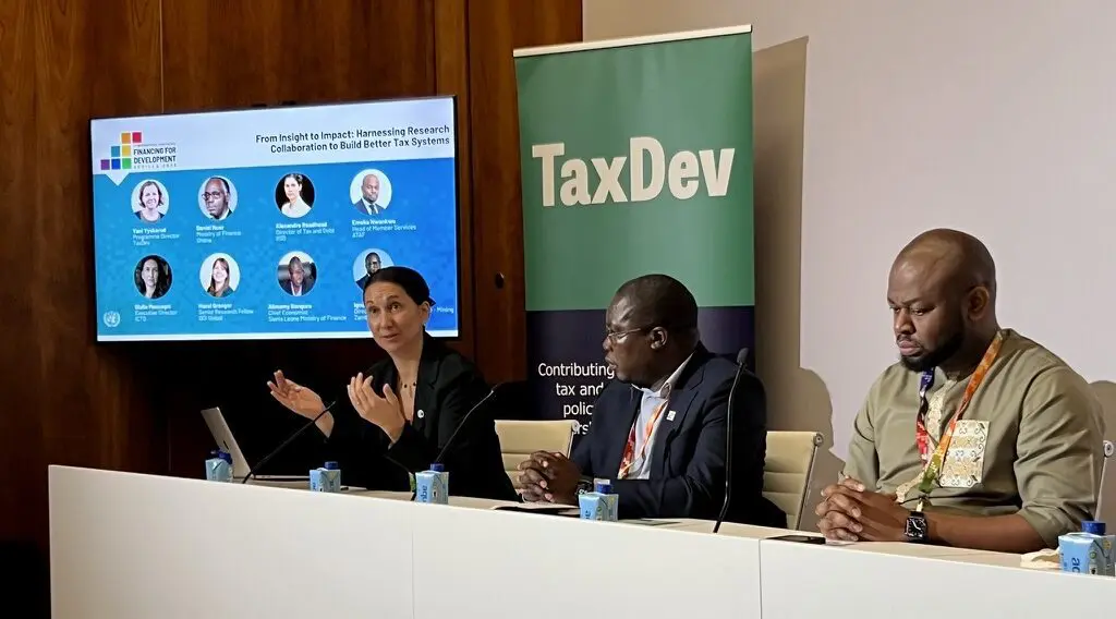Panel of speakers at a TaxDev side event, with a screen showing speaker photos
