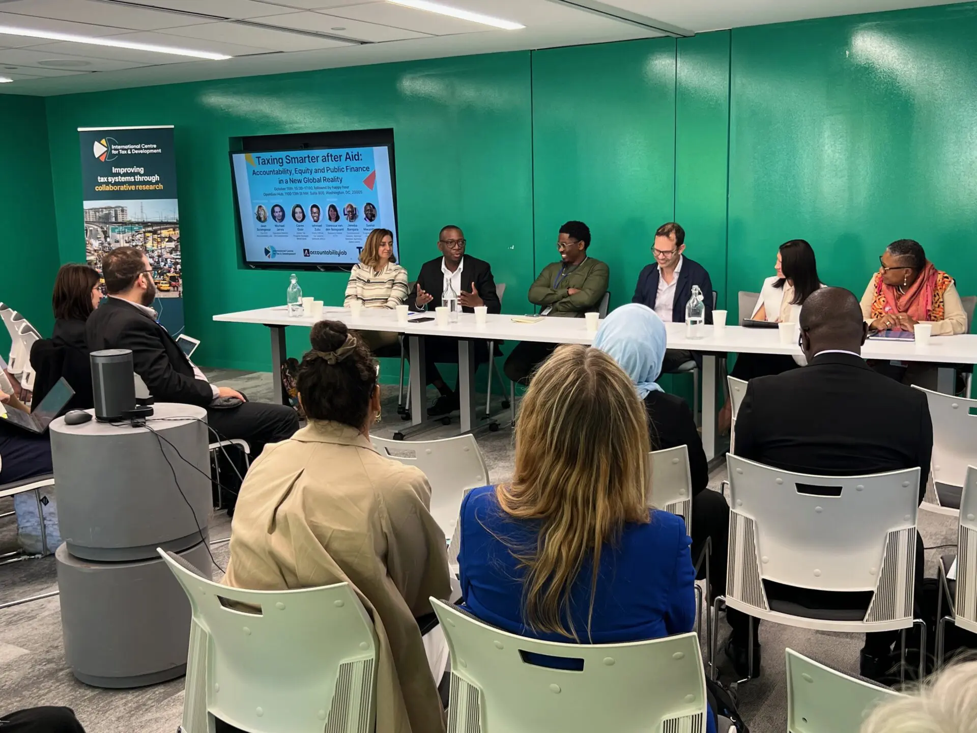 Panel of speakers at a long table facing the audience at the Taxing Smarter after Aid event