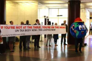 Campaigners holding a banner: If you're not at the table, you're on the menu. UN tax body now