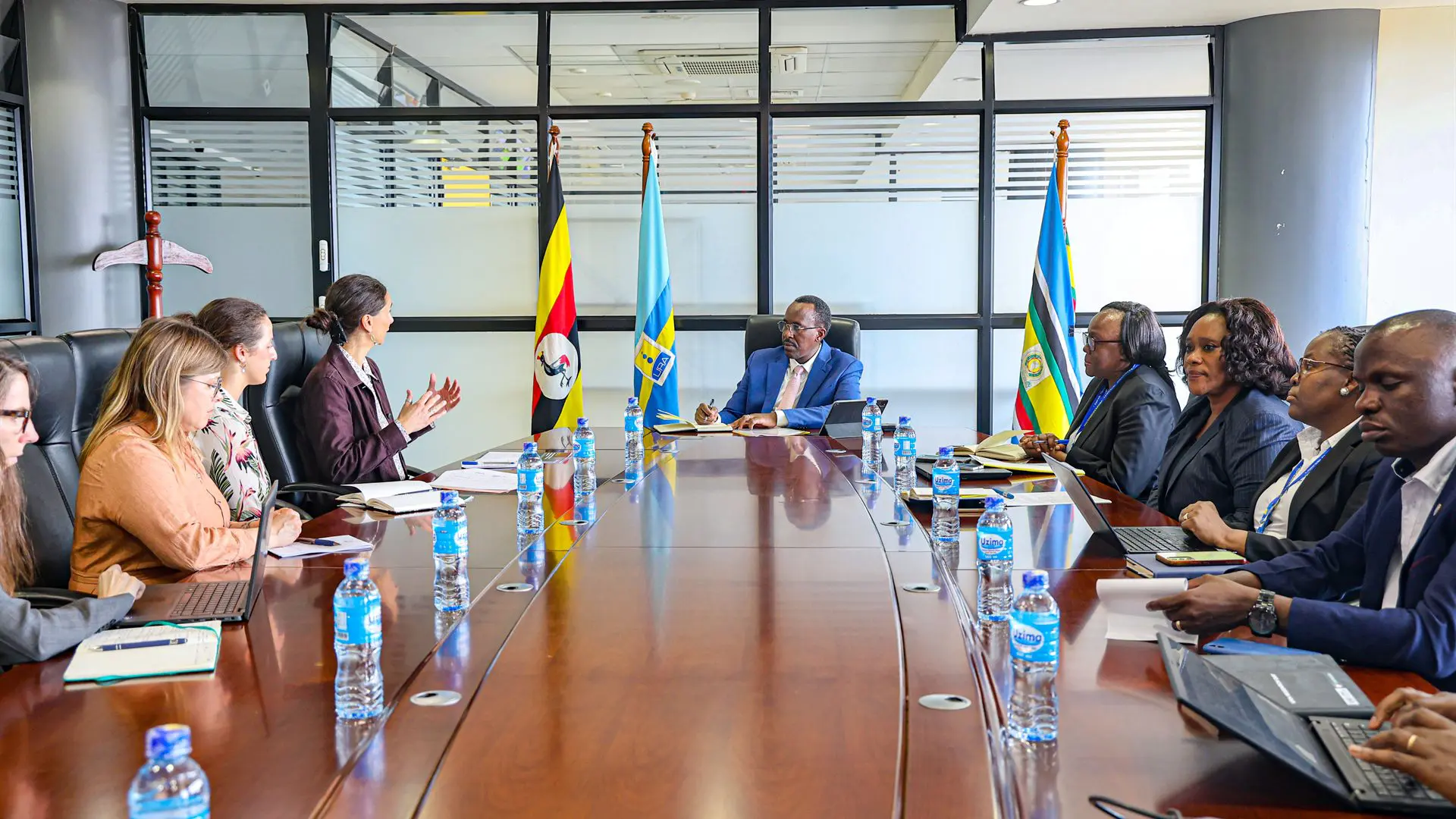 Chercheurs de l'ICTD en réunion avec des responsables autour d'une table de conférence, devant les drapeaux de l'Ouganda et de la Communauté d'Afrique de l'Est