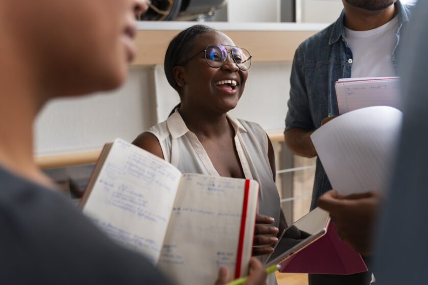 Group of people standing in a circle holding notebooks and tablets, only one face is clearly showing