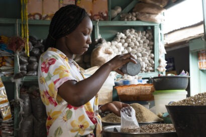 A woman stands in the middle of a small convenient stall, measuring grains.