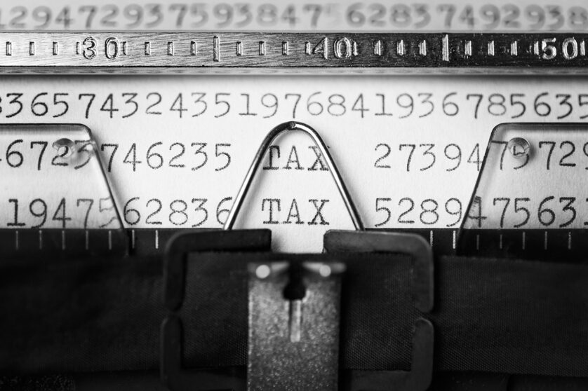 Closeup on a paper hanging from a typewriter, with the word TAX highlighted among a series of numbers